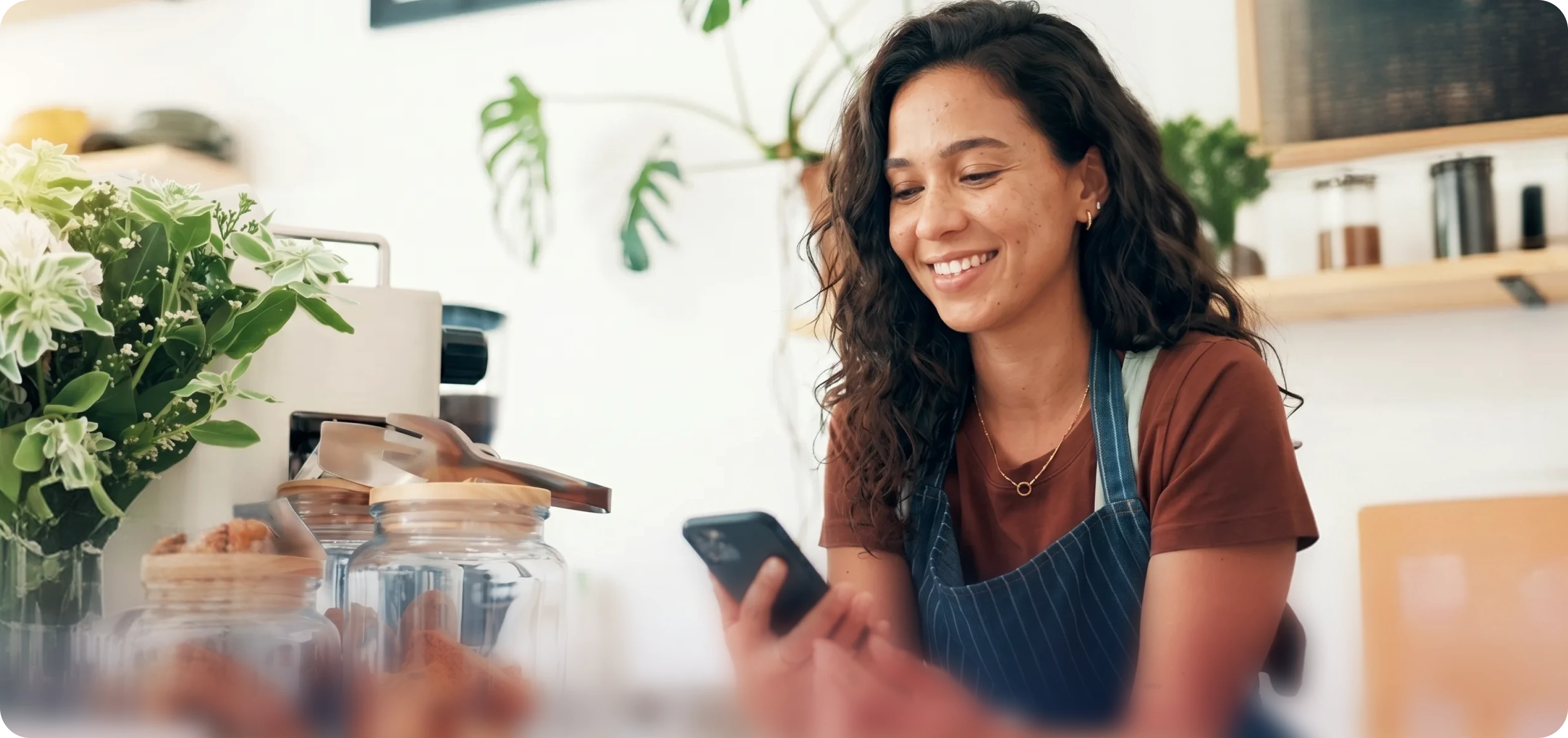 Graphic showing a smiling female employee with curly hair, wearing an apron, looking down at a smartphone in her hands.