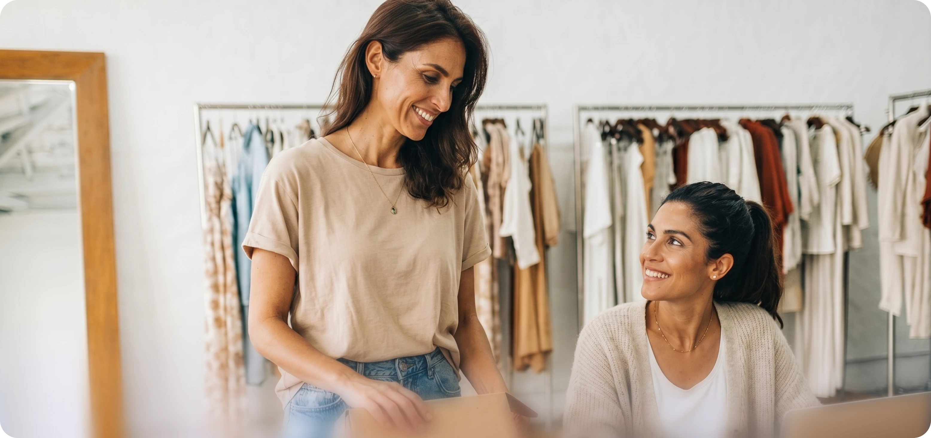 Graphic showing two smiling female coworkers interacting in a clothing boutique, with clothing racks visible in the blurred background.